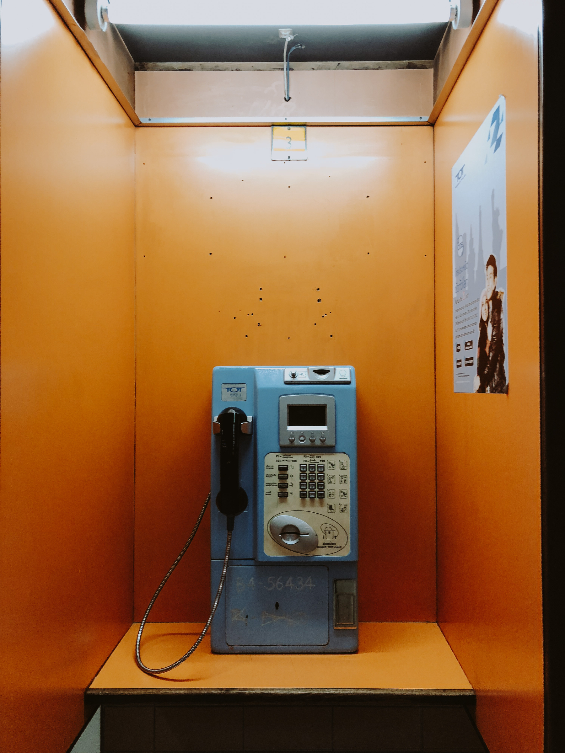 A blue pay phone, on an orange booth. 