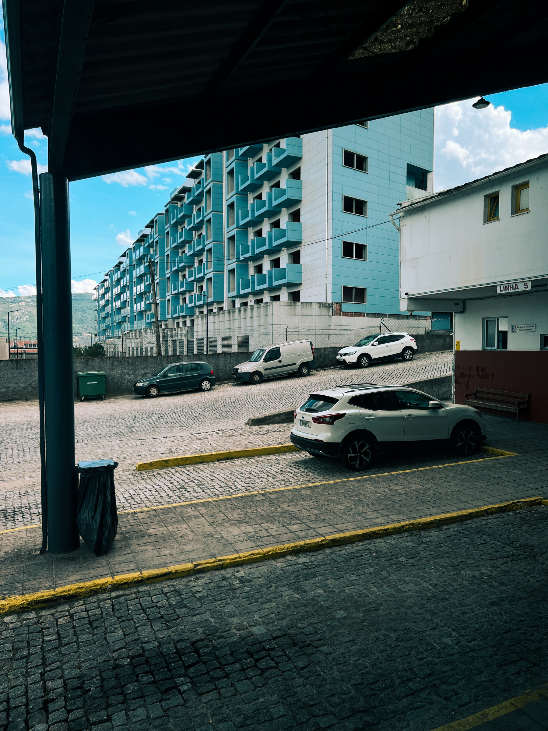 A car is parked inside a bus depot. Ugly blue building in the back. 