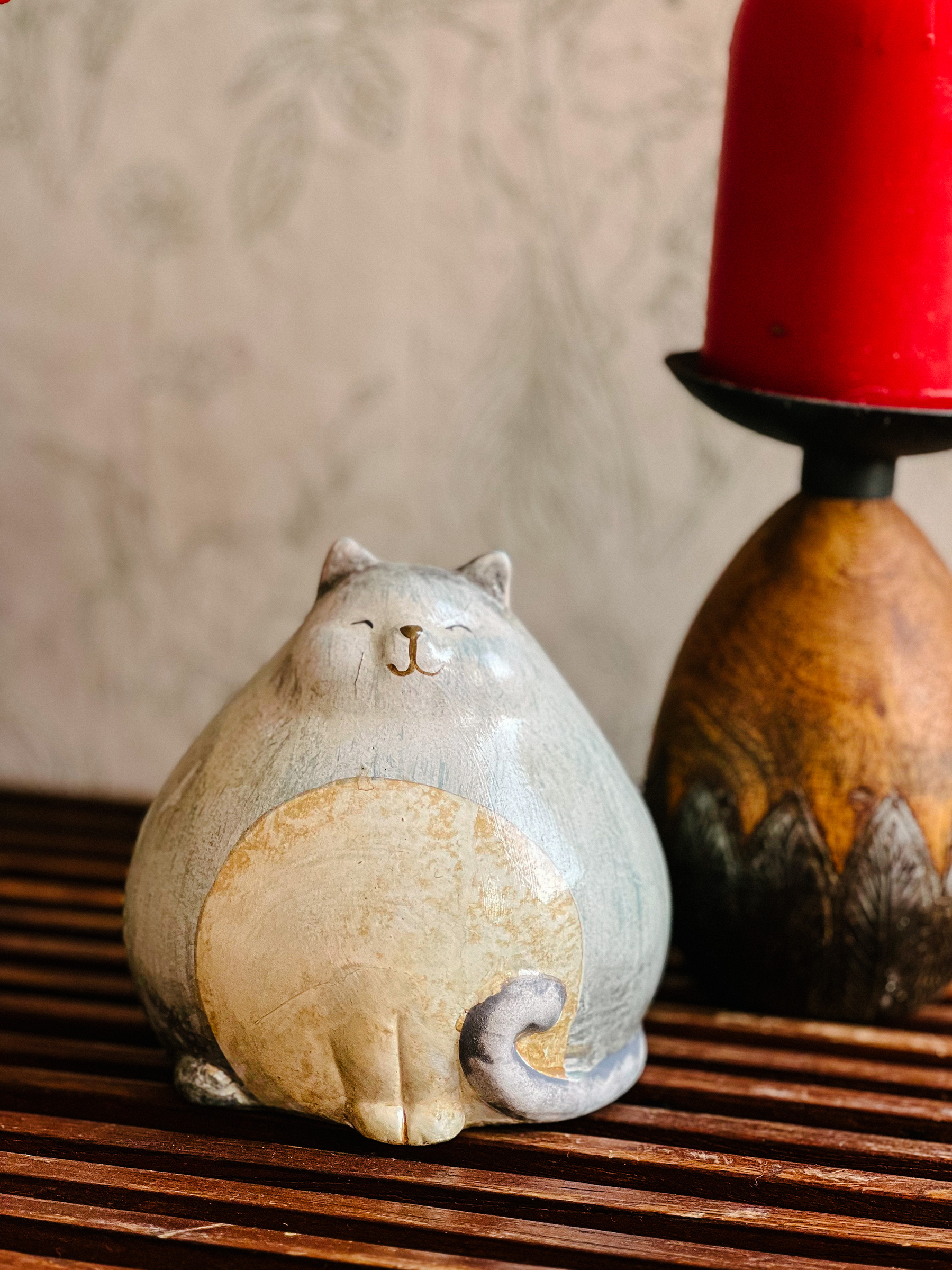 A smiling porcelain cat sitting next to a red candle. 