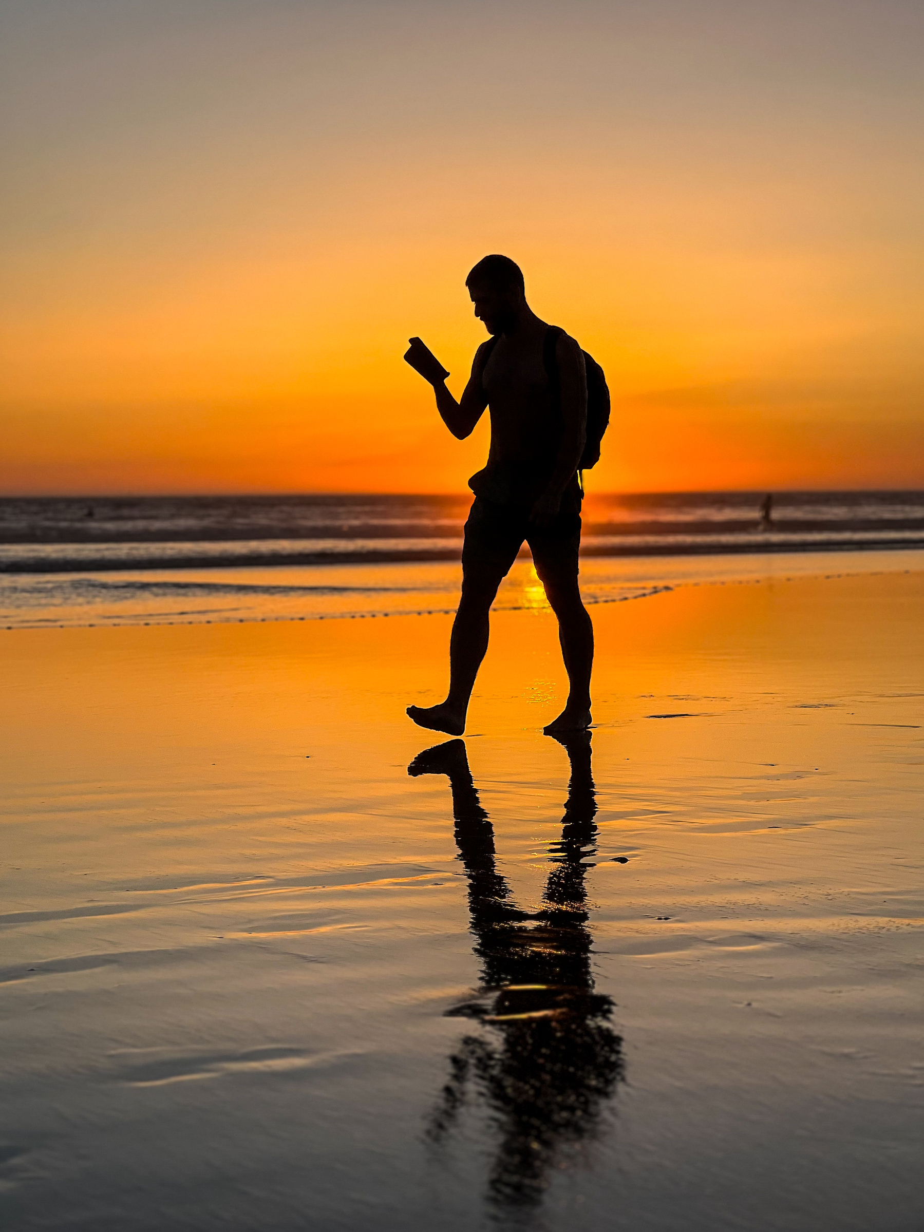 a man walks on the beach, while the sun sets.