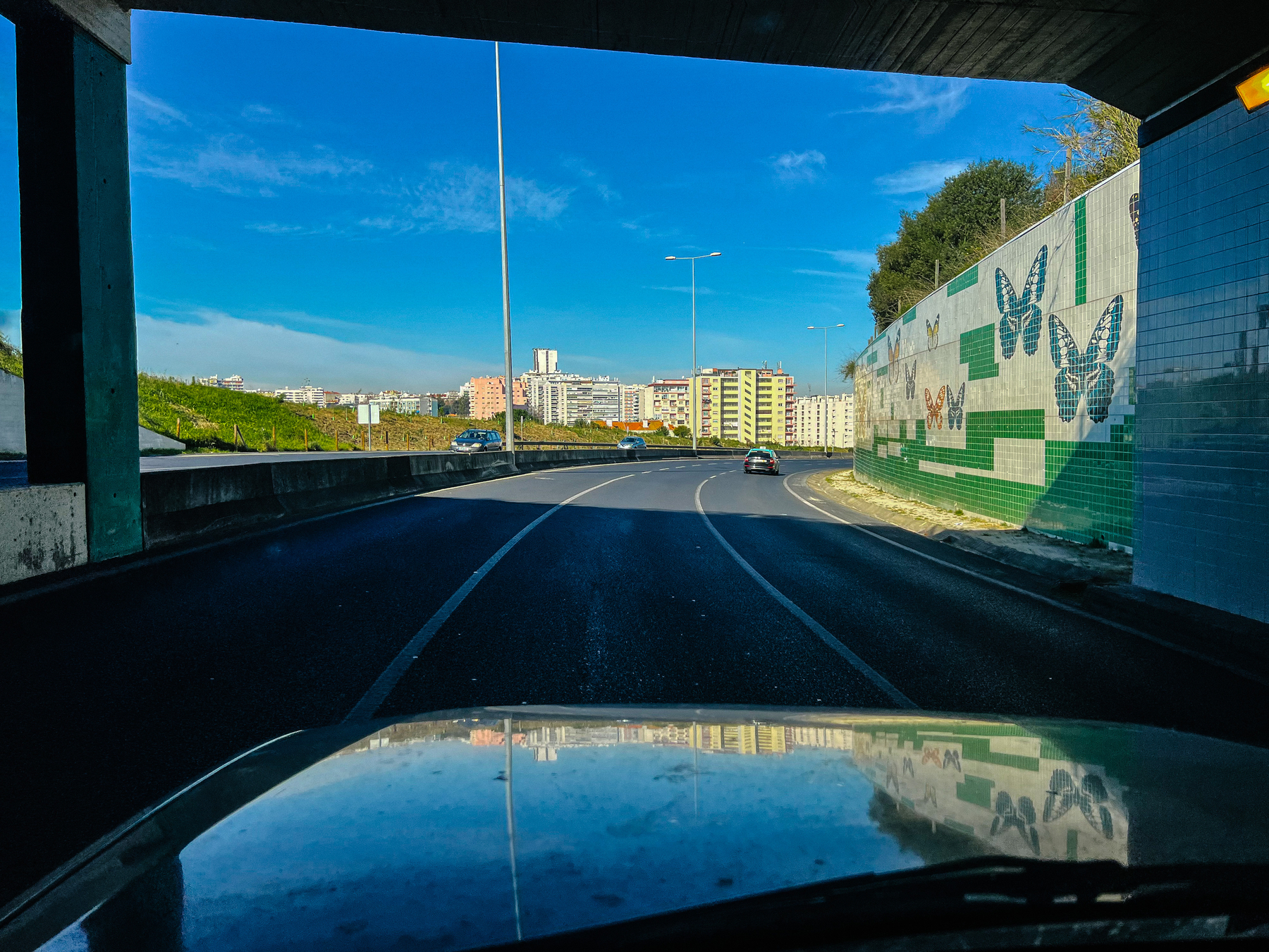 blue skies ahead on a road, buildings at the distance, and some butterflies on a tile panel on the right side 