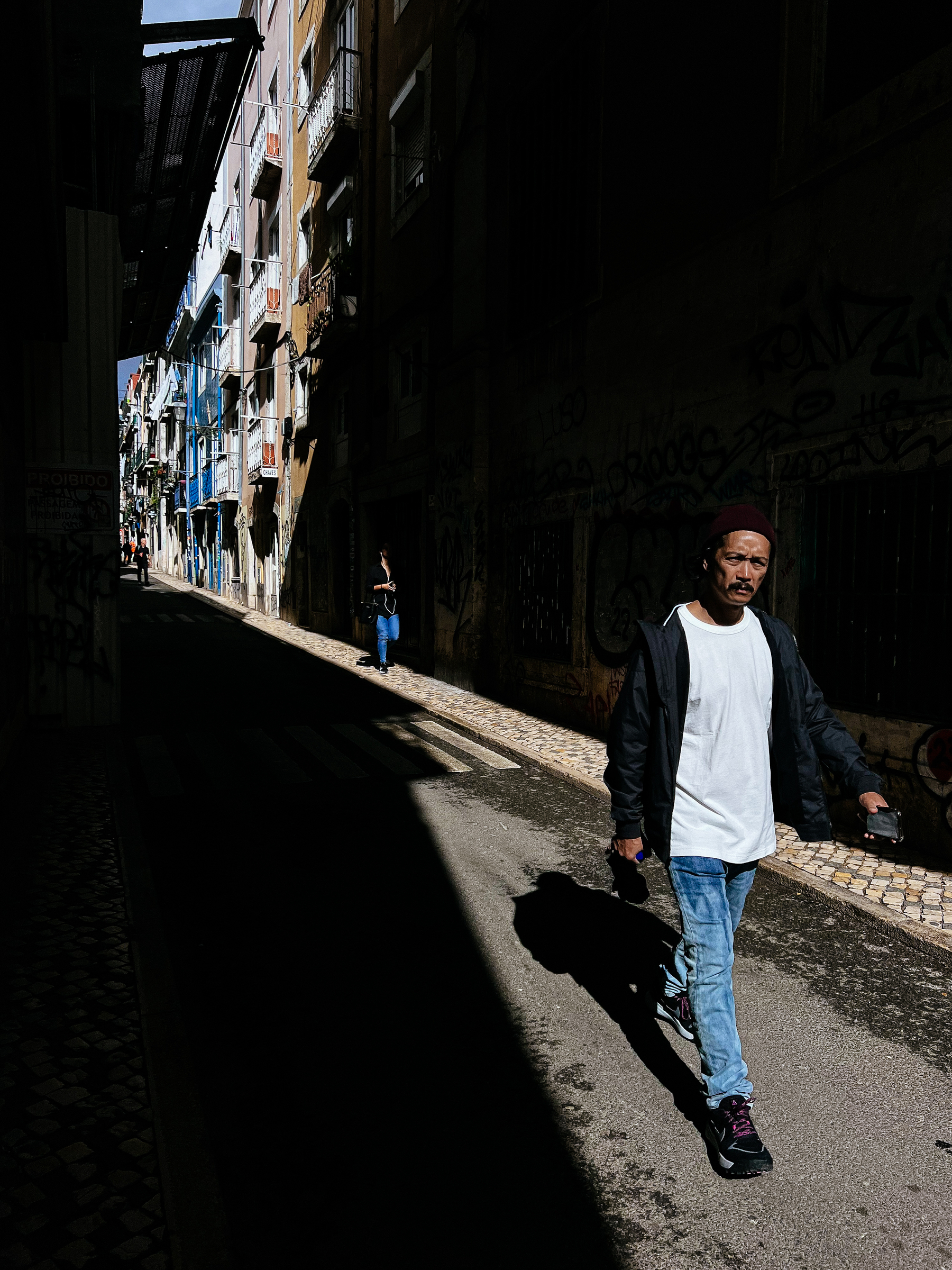 A man walks by, on a dramatically shaded narrow street.