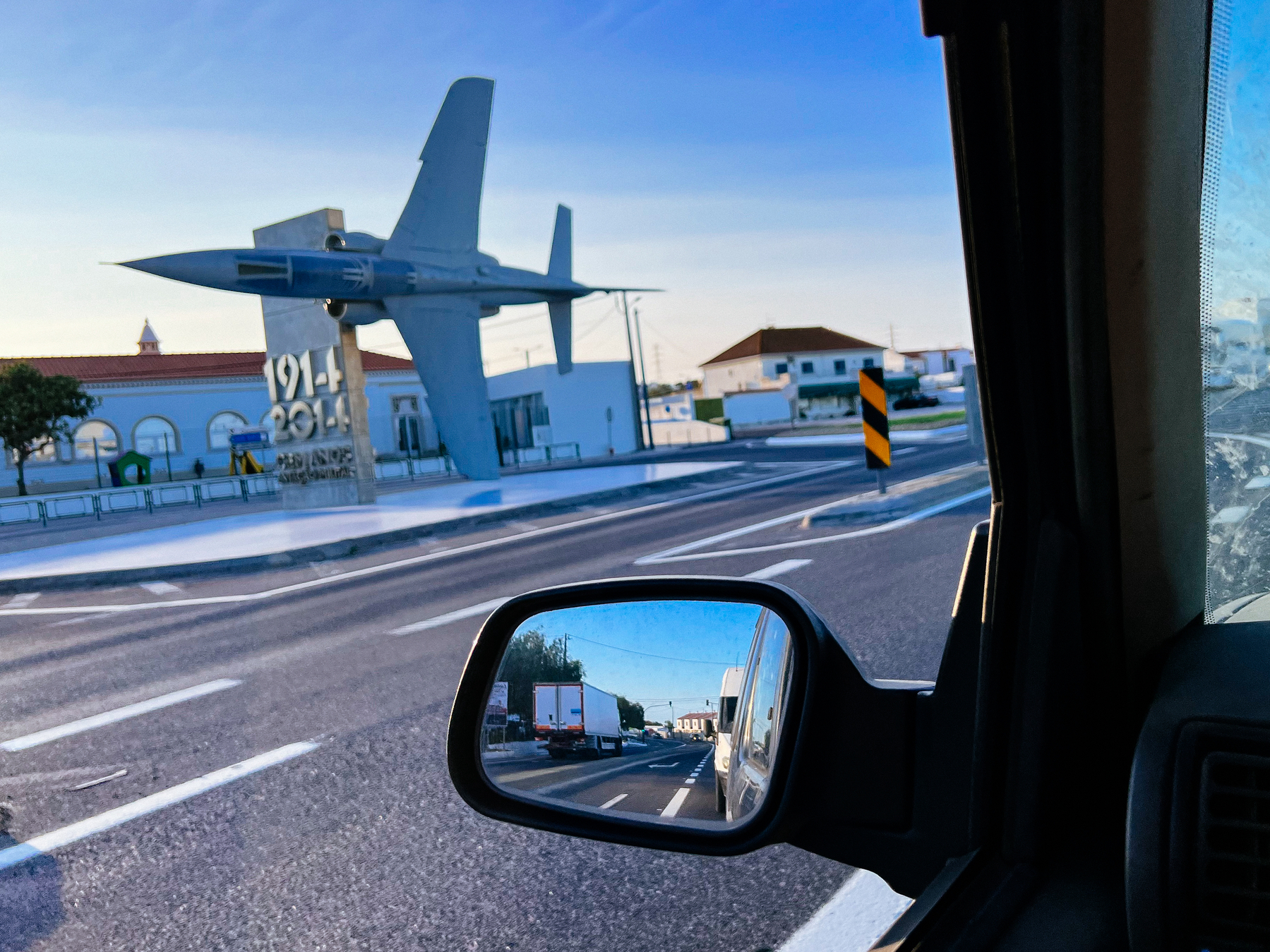 A fighter jet by the side of the road, seen from inside a car. 