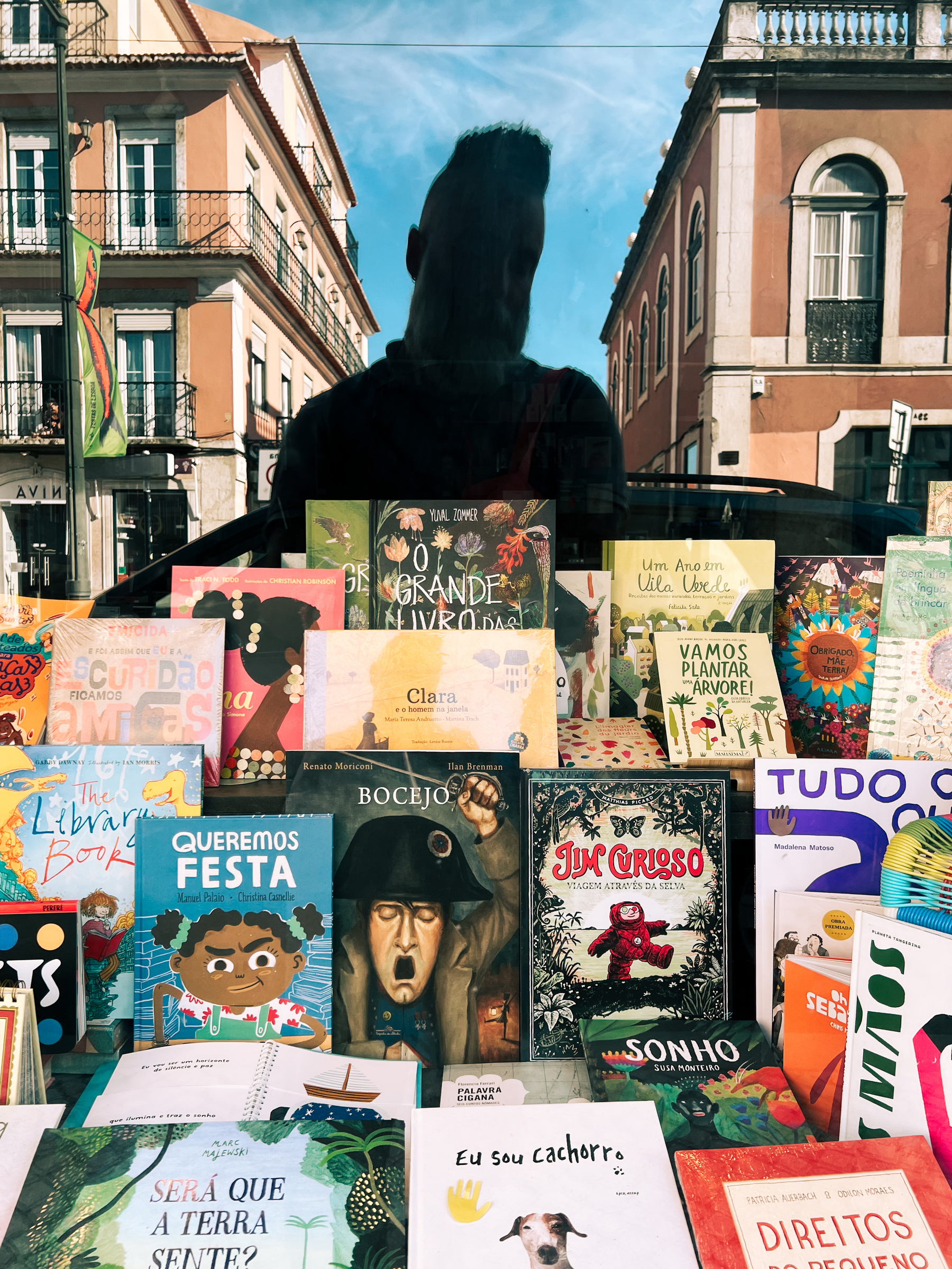 A man’s reflection on a bookstore window, filled with children’s books. 