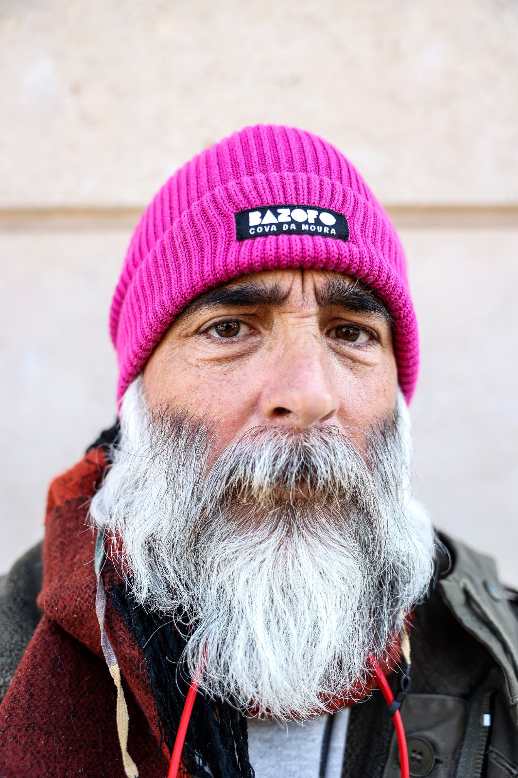 A bearded man looks at us, wearing a pink beanie. 