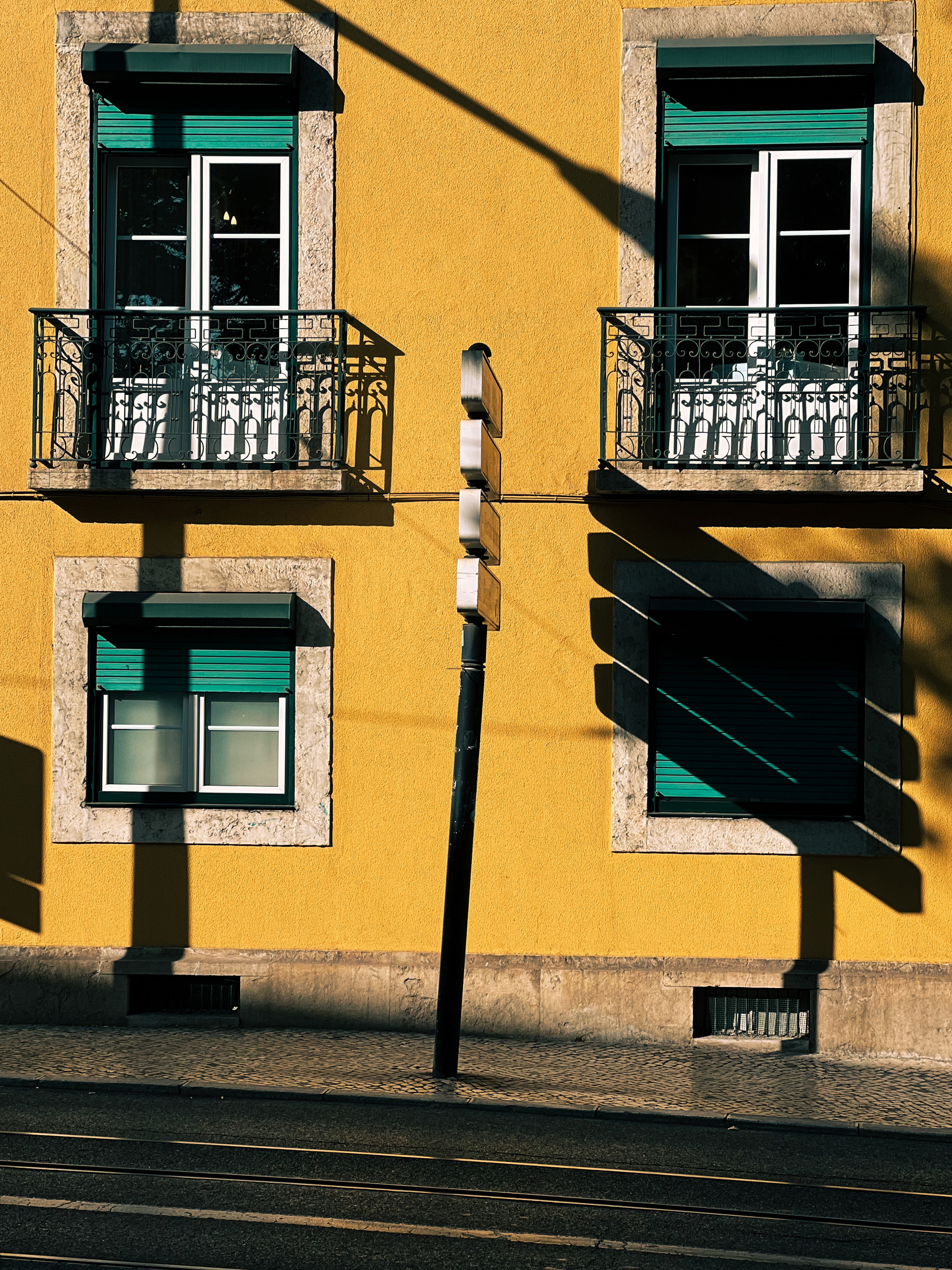 A street sign casts a long shadow over a yellow building. 