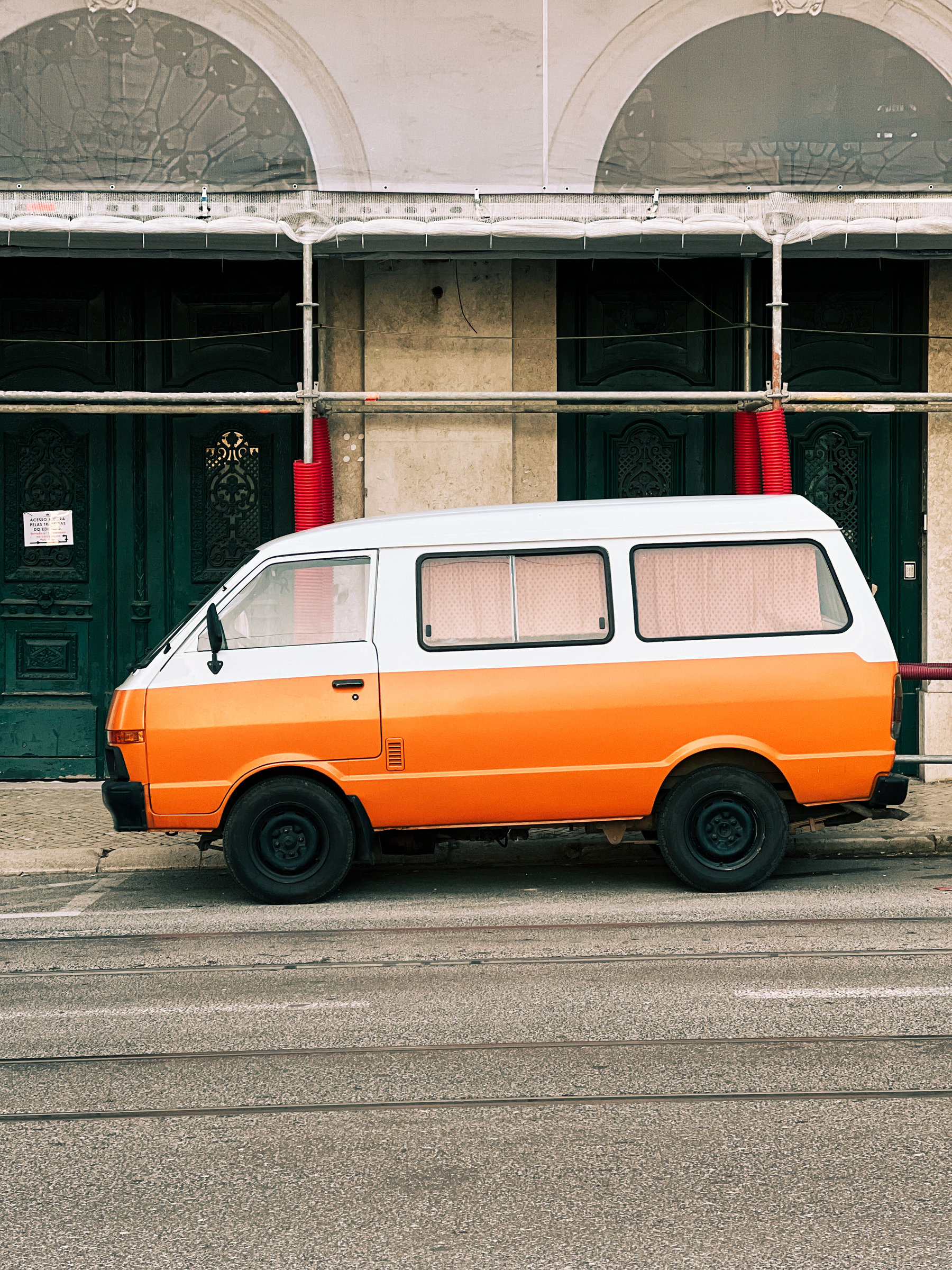 An orange and white van, parked in front of a building undergoing renovation.