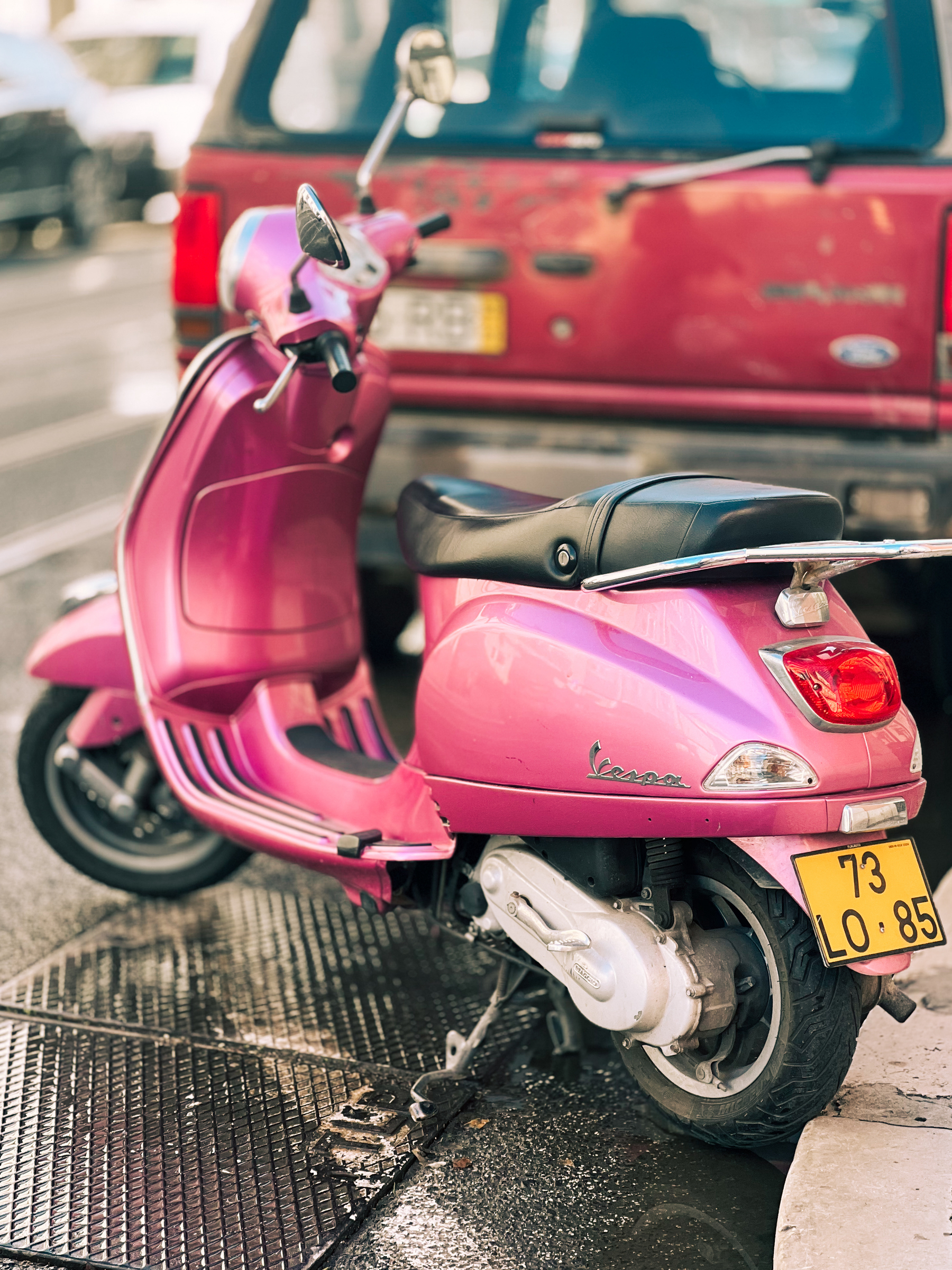 A pink scooter parked behind a red truck.