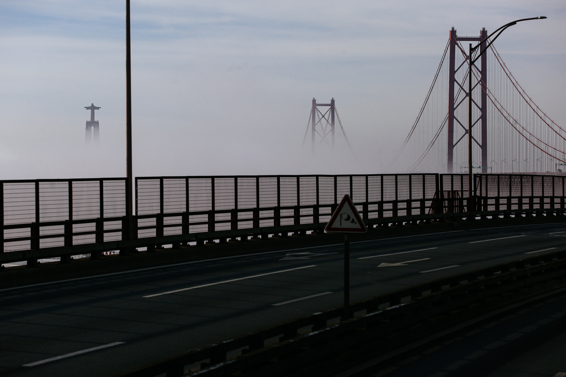 a statue and a bridge rise from the fog