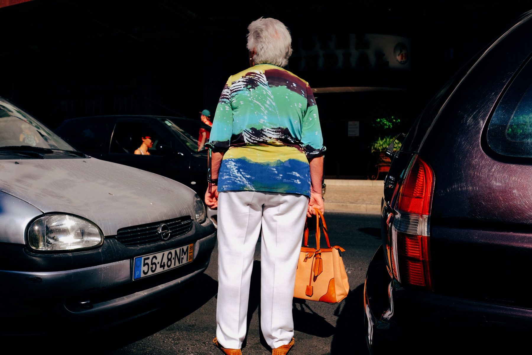 a woman with a very colourful shirt crosses the street.