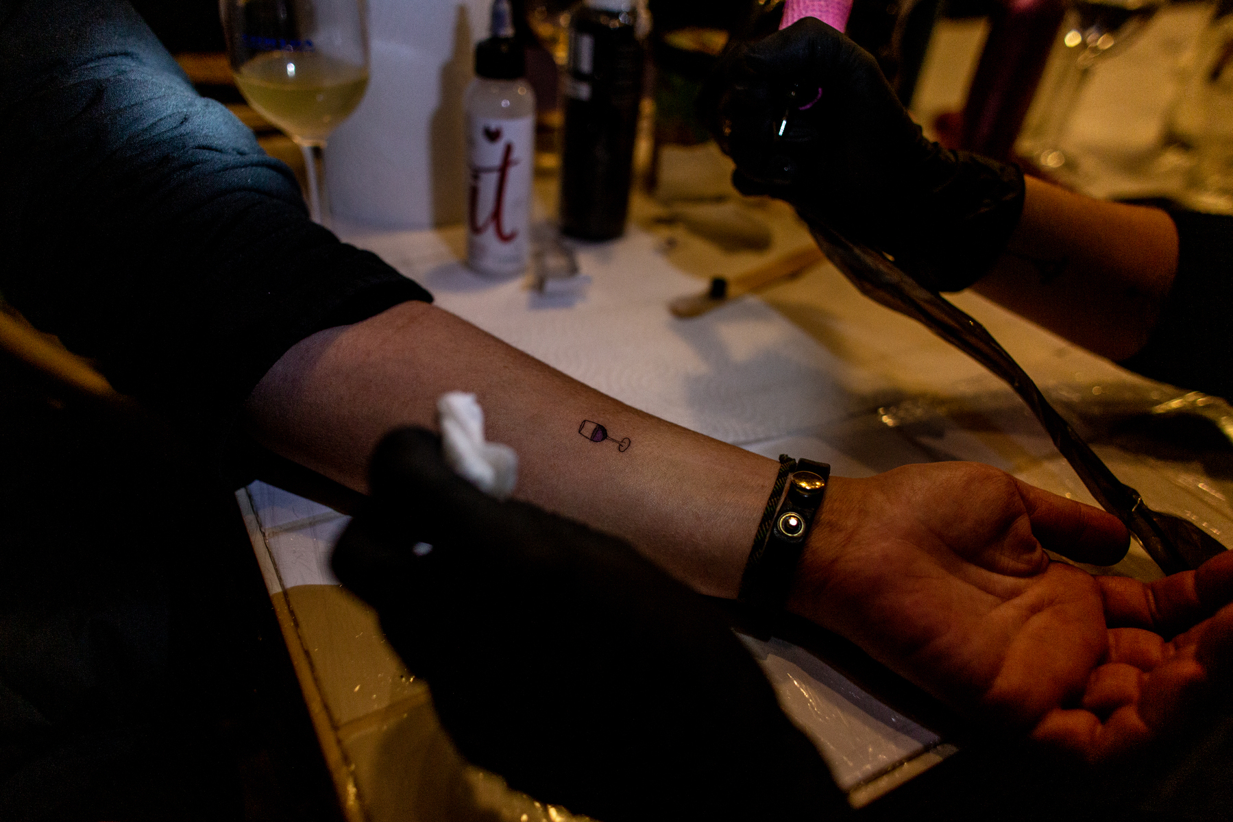 an arm is getting a tiny glass of wine tattoo