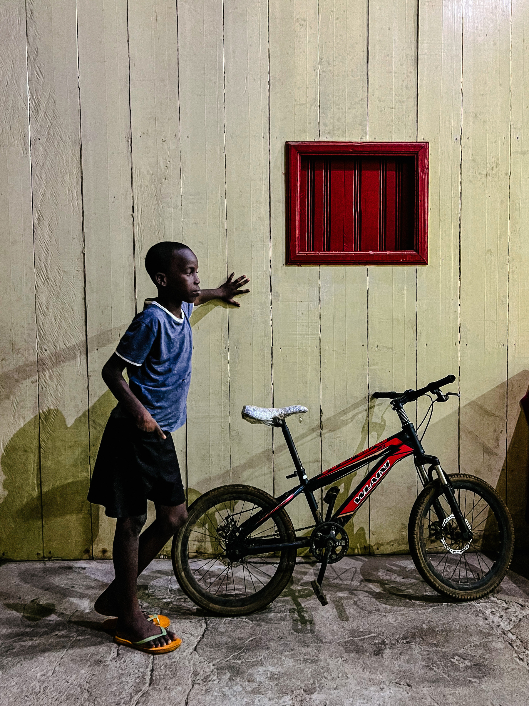 A boy leans against a wall, his bicycle by his side. 