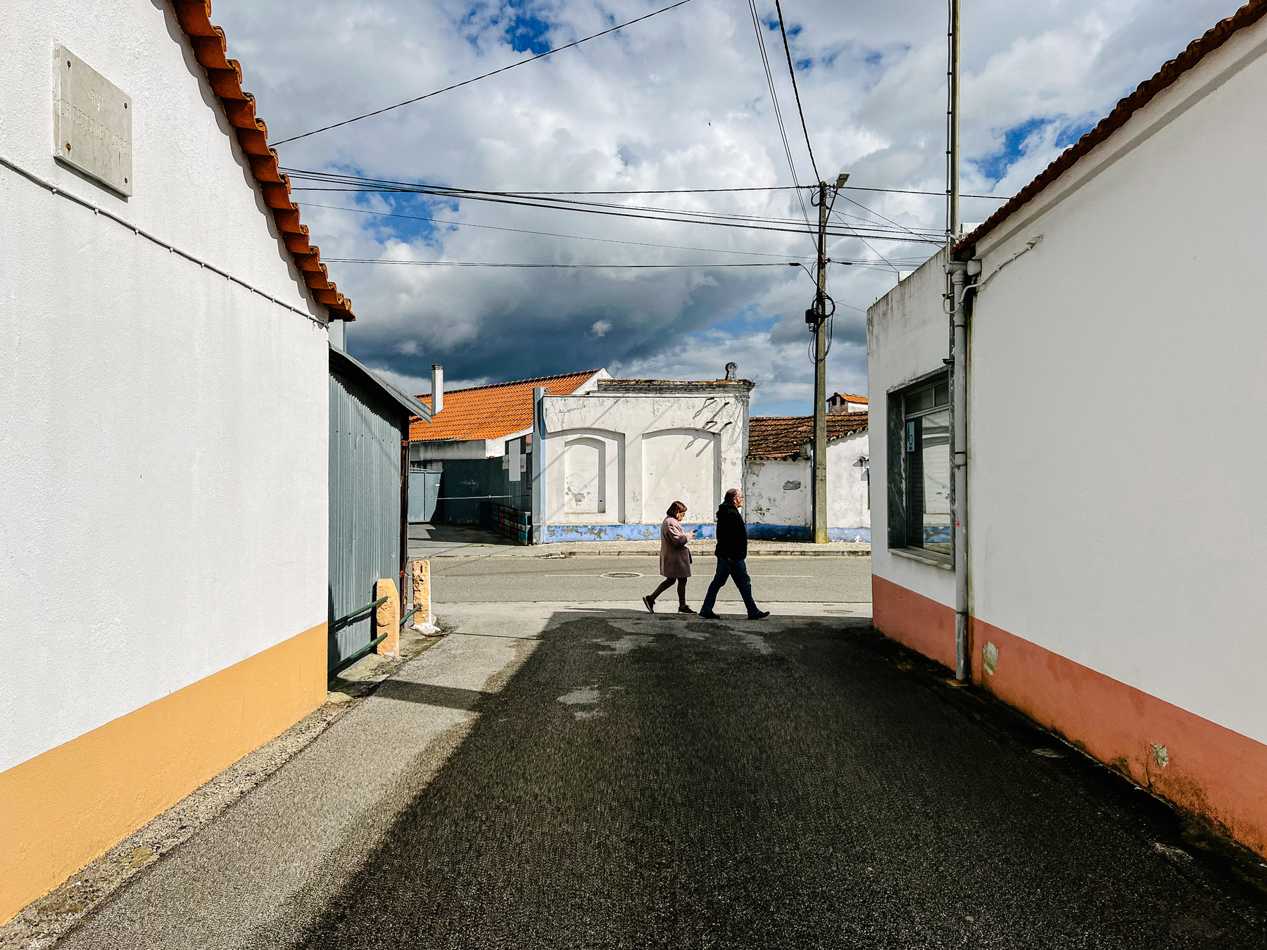 A couple is seen walking outside, surrounded by houses. Cloudy sky. 
