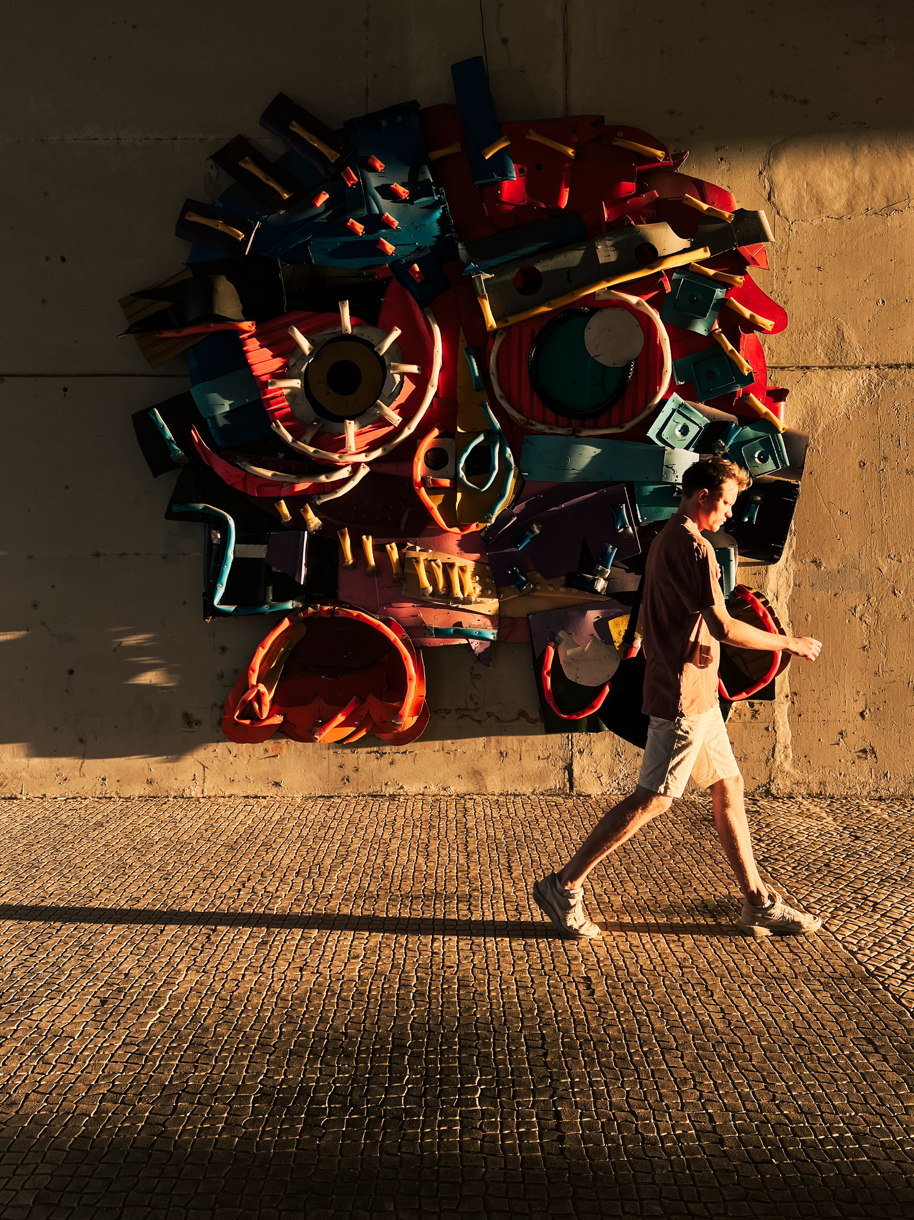 Street art. A man walks by a sculpture on a wall.
