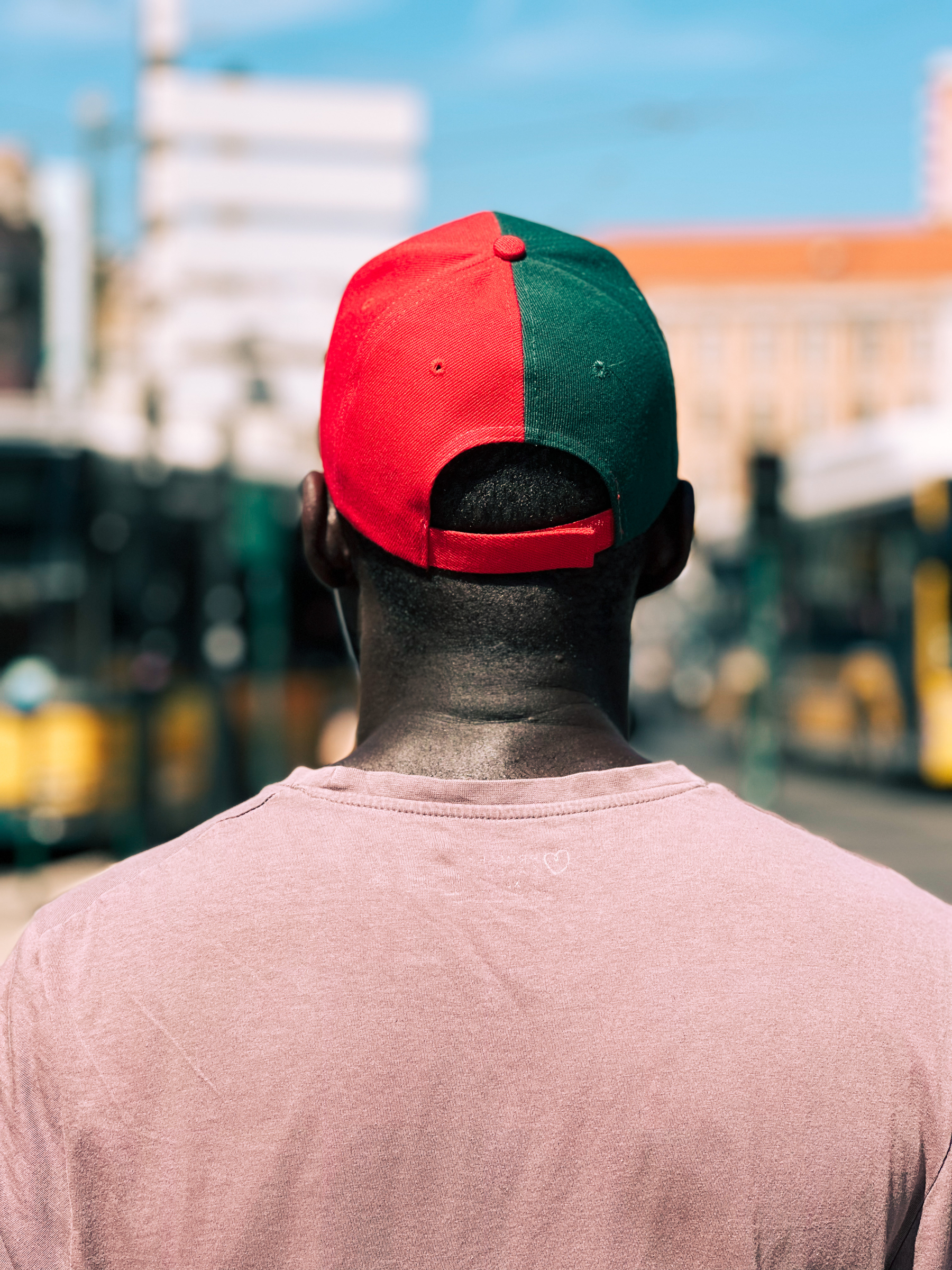 A man shot from the back, wearing a cap. Half the cap is red, other half green. The Portuguese flag. 