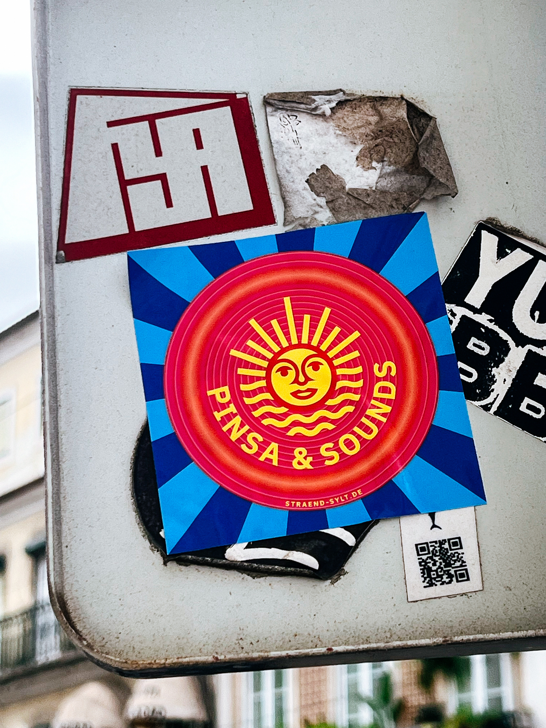 “PINSA&amp;SOUNDS”, on a round sticker, with a smiling sun and the sea. 