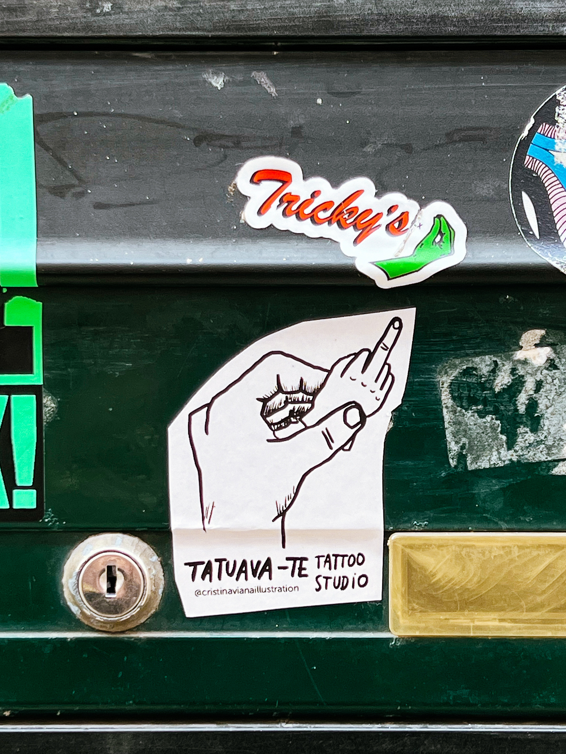 A sticker that is an ad for a tattoo studio, as many of them are. Done in &ldquo;tattoo style&rdquo; drawing. A hand carefully holds another, smaller, hand. This second hand is giving us the finger. On top of that, unrelated but well placed, is the word &ldquo;Tricky&rsquo;s&rdquo;, and yet another hand. A green one, in the &ldquo;Italian speaking&rdquo; style.