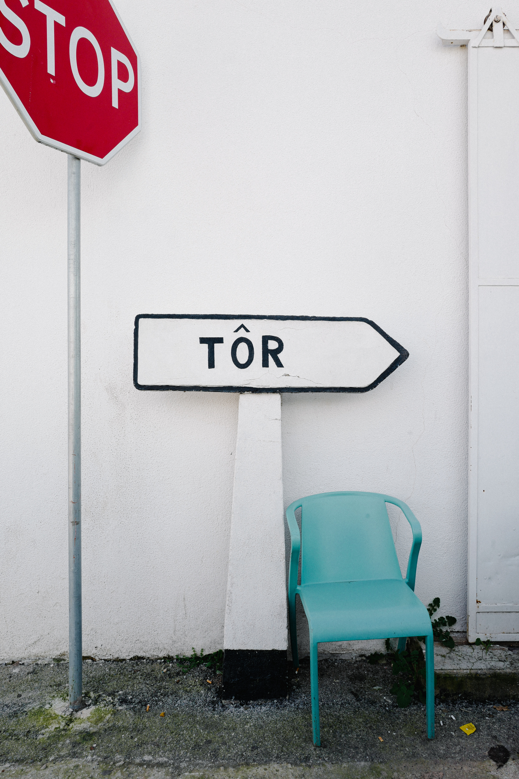 A stop sign, a directional arrow sign with the word "TÔR," and a single turquoise chair against a white wall.